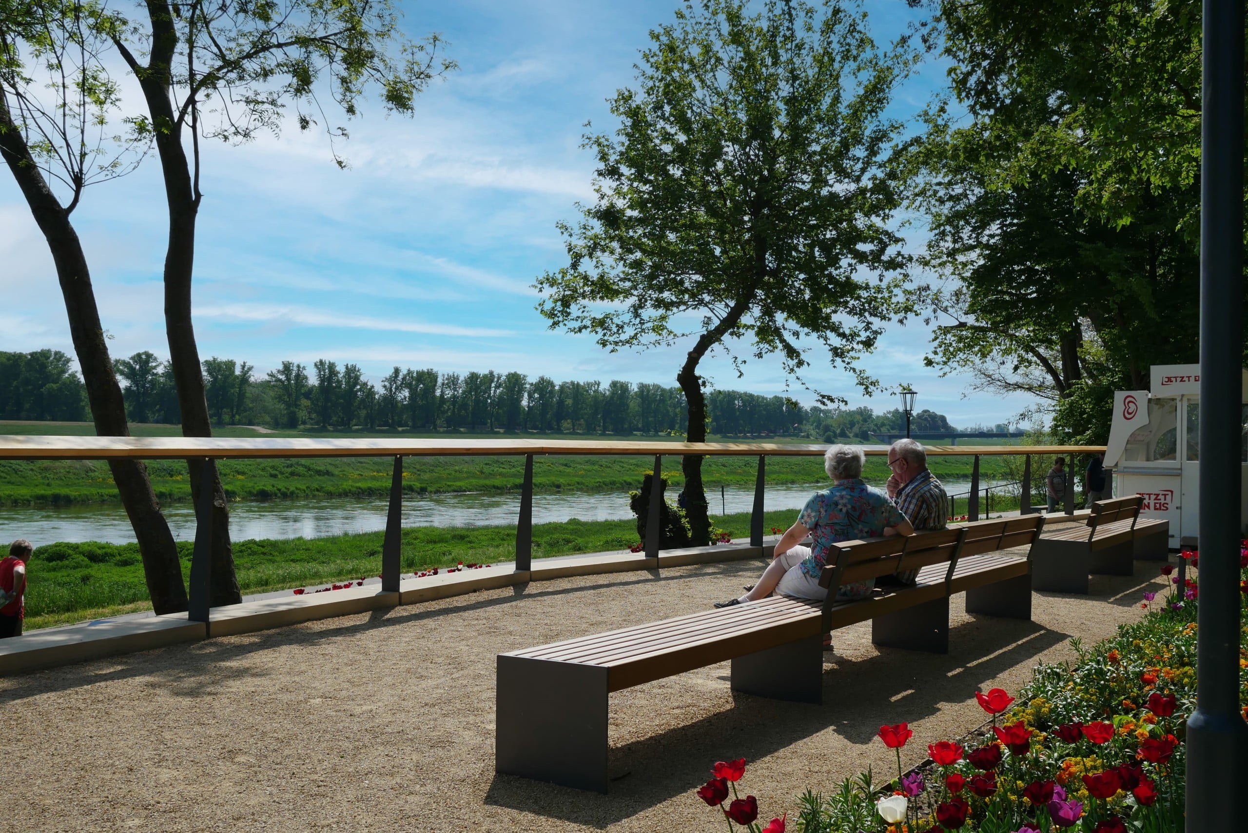 Ein Weg an einem Fluss, mehrere Sitzbänke, eine Geländer mit Holz grenzt den Fluss ab. Elbbalkon, Foto: Landesgartenschau Torgau