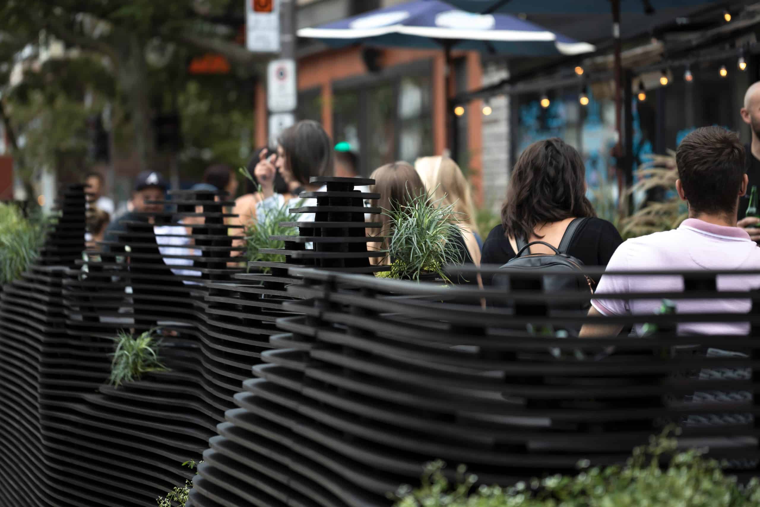 Gäste sitzen in dem Außenbereich eines Restaurants, einem Parklet aus schwarzem Holz in geschwungenen Formen. Quinzhee Architecture und atelier mock/up, Parklet Miyagi, Québec, Foto: 1Px