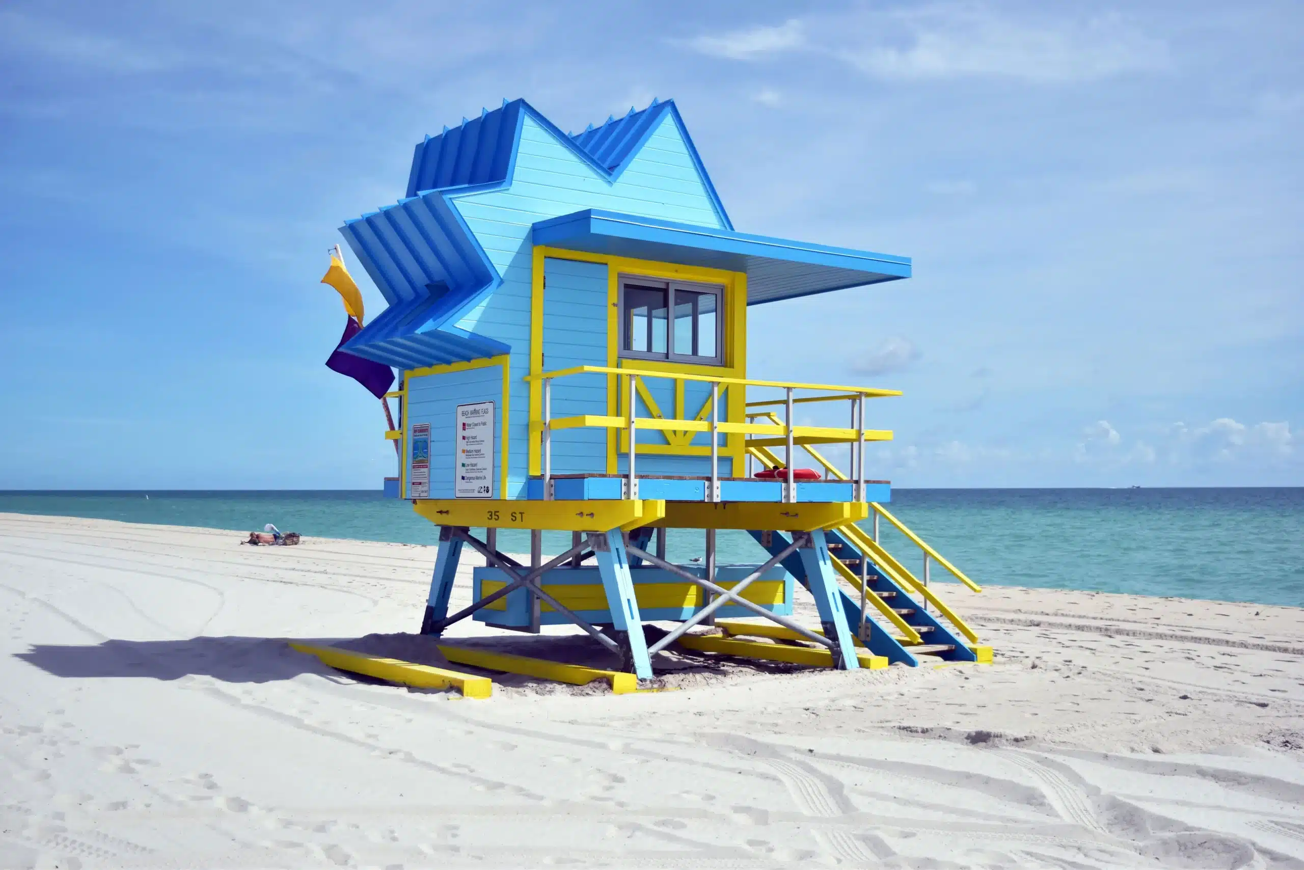 Ein hölzernes Wachhäuschen mit gezacktem Dach in Blautönen und Gelb am Strand. Miami Beach, Lifeguard Tower, William Lane, Foto: Archiv Architekten