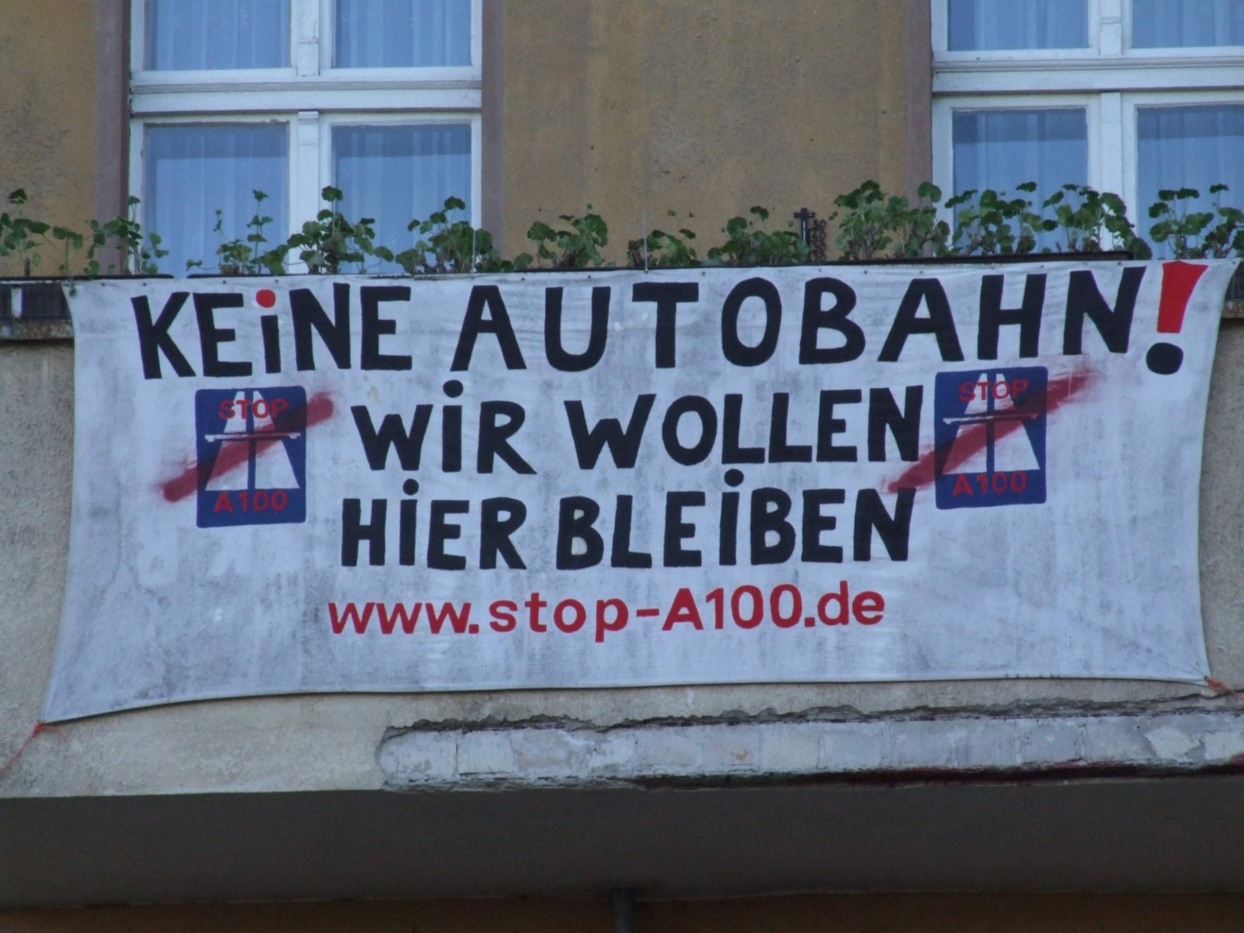 Auf einem weißen Banner steht in schwarzer Schrift der Slogan: Keine Autobahn - wir wollen bleiben.