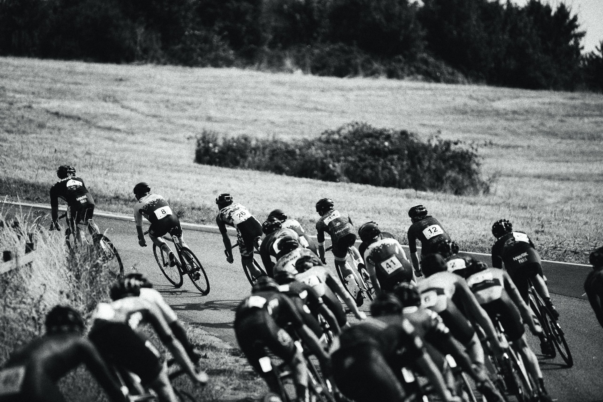 Eine Gruppe von Radrennfahrern geht in eine Linkskurve, Aufnahme in Schwarz-Weiß. Foto: Jonny Kennaugh via Unsplash