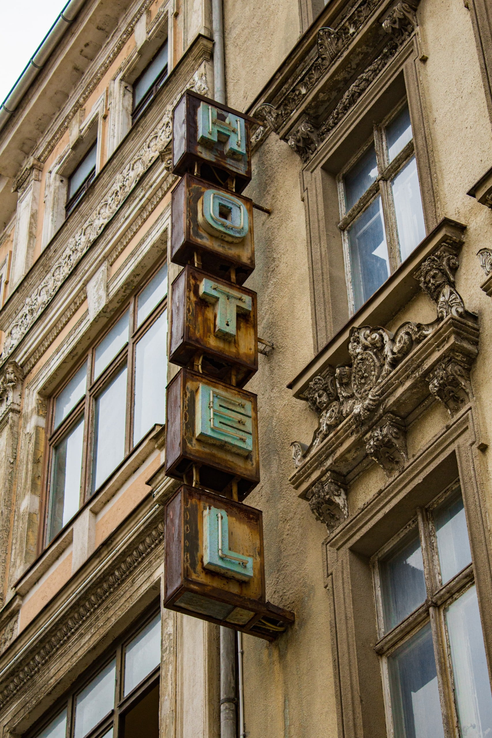 Vor einer Altbaufassade hängt eine Leuchtreklame mit der Schrift Hotel. Es wirkt heruntergekommen