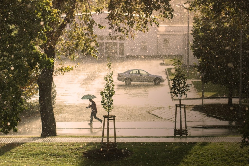 Eine Straße im Regen, ein Mann mit Regenschirm rennt über den Gehweg, im Hintergrund fährt ein Auto vorbei. Der Klimawandel ist inzwischen in allen Kommunen spürbar. Foto: Gundula Vogel via Pixabay
