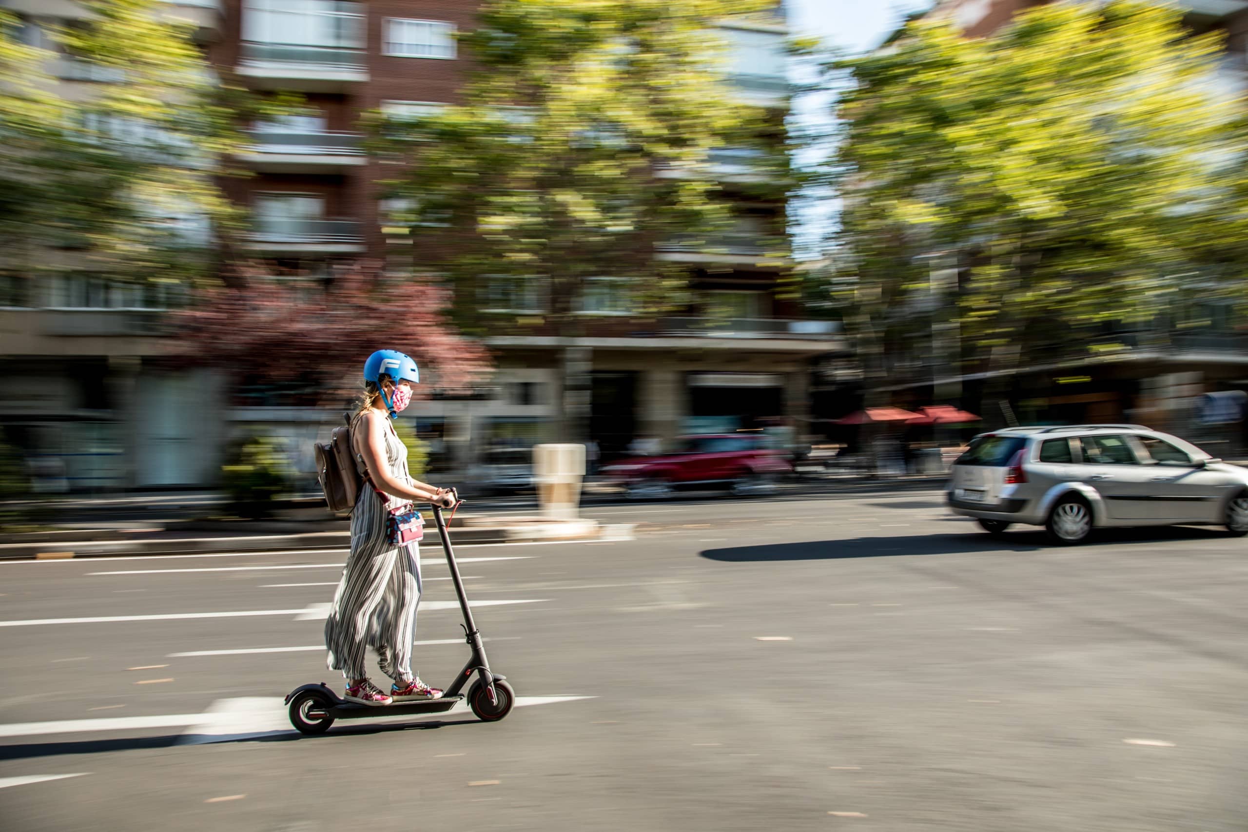 Eine Frau mit Helm fährt auf einem E-Tretroller über eine Straße.